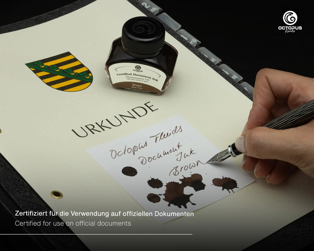 A hand holds a fountain pen over an off-white document, writing with a brown ink sample. An octopus brand document ink bottle labeled 'Brown' sits nearby on a dark surface, with additional sample ink spots and German certification text visible.