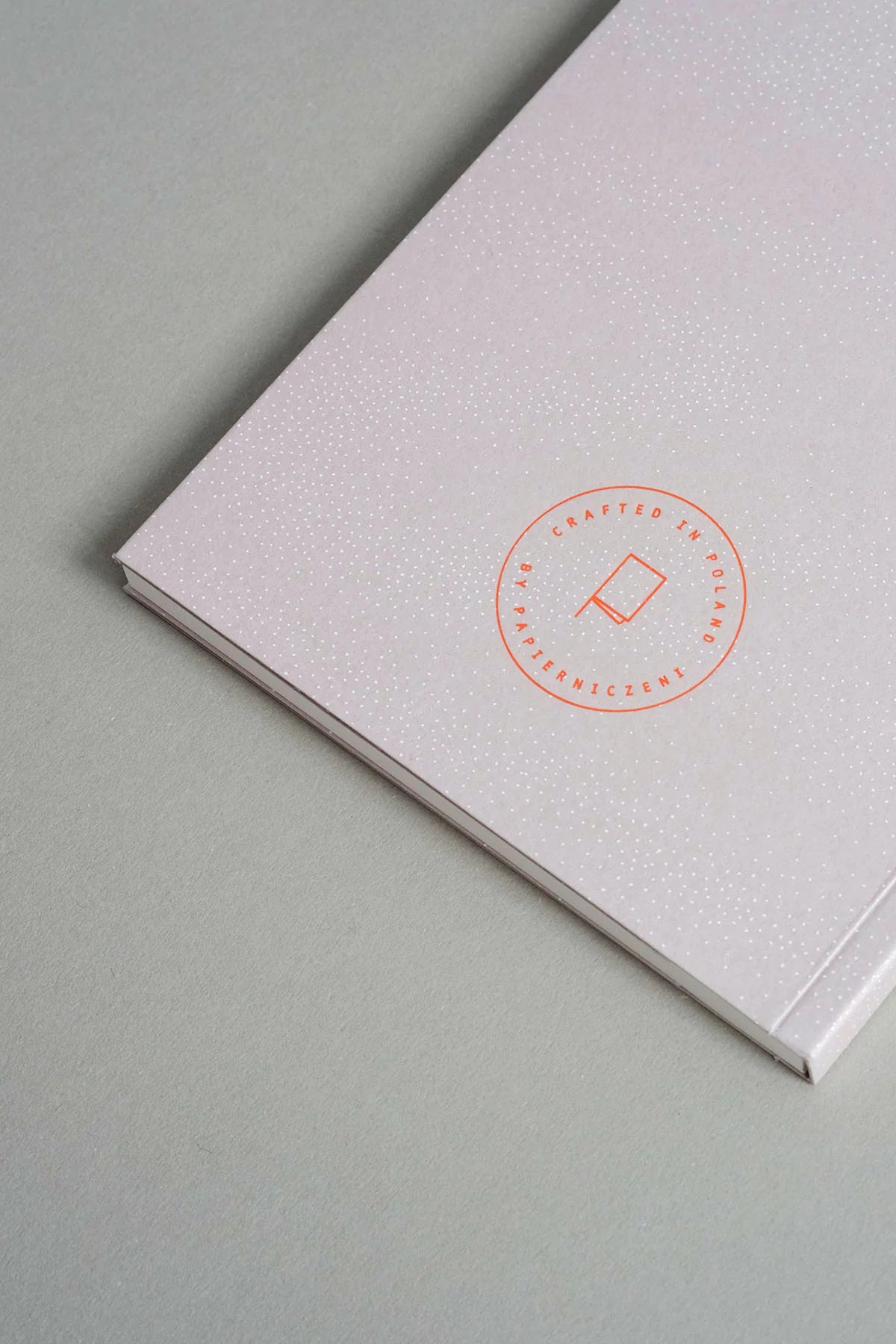 A close-up of a textured white notebook or journal with a circular orange-red foil stamp reading 'Crafted with Love' and a small heart, placed on a light gray surface. Papierniczeni Luna Notebook - Full Moon back cover
