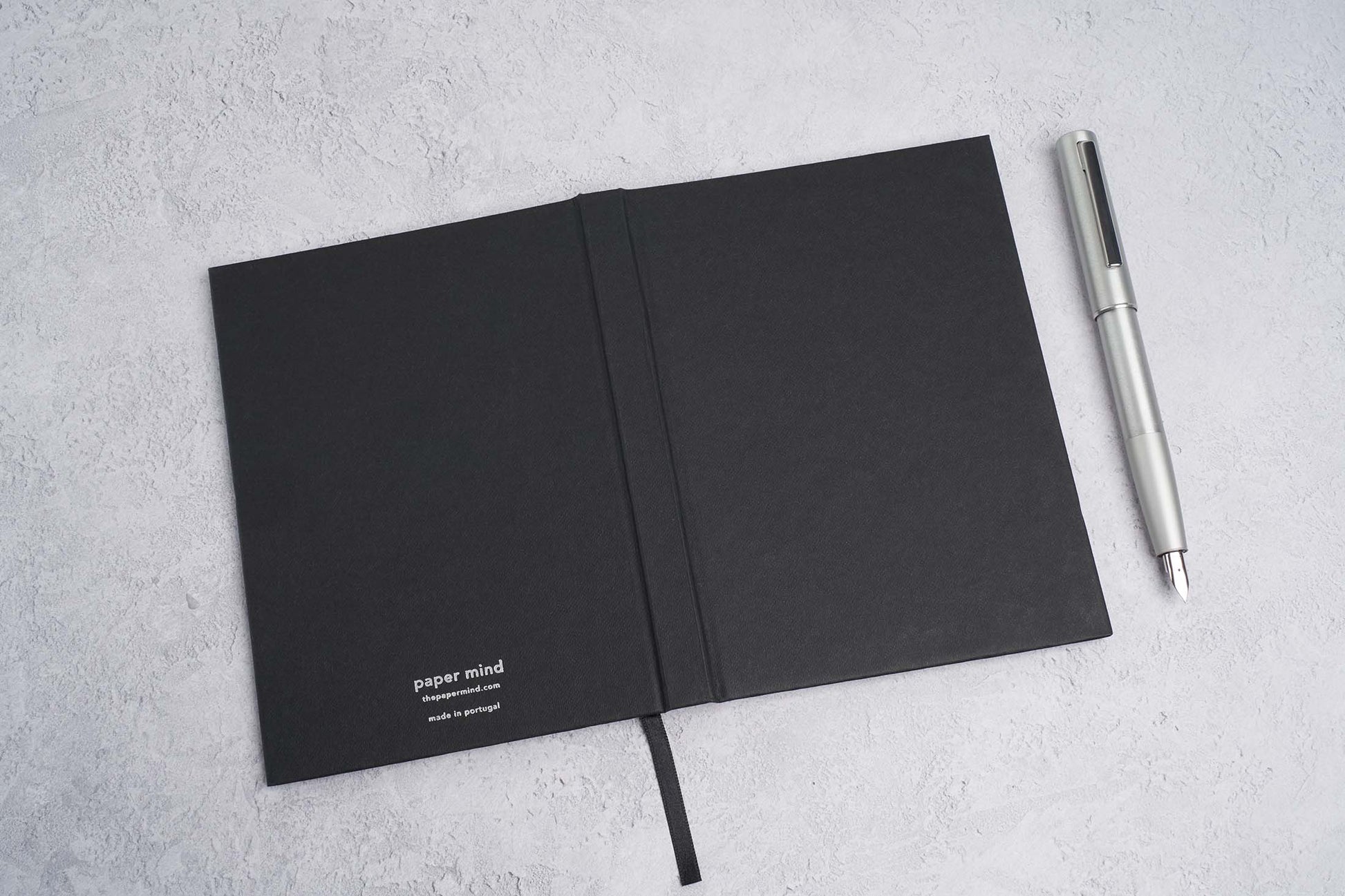 blocker paper notebook in black laying face down on a gray surface with a Lamy Aion fountain pen in silver. ultra premium notebook. notebook for fountain pens 