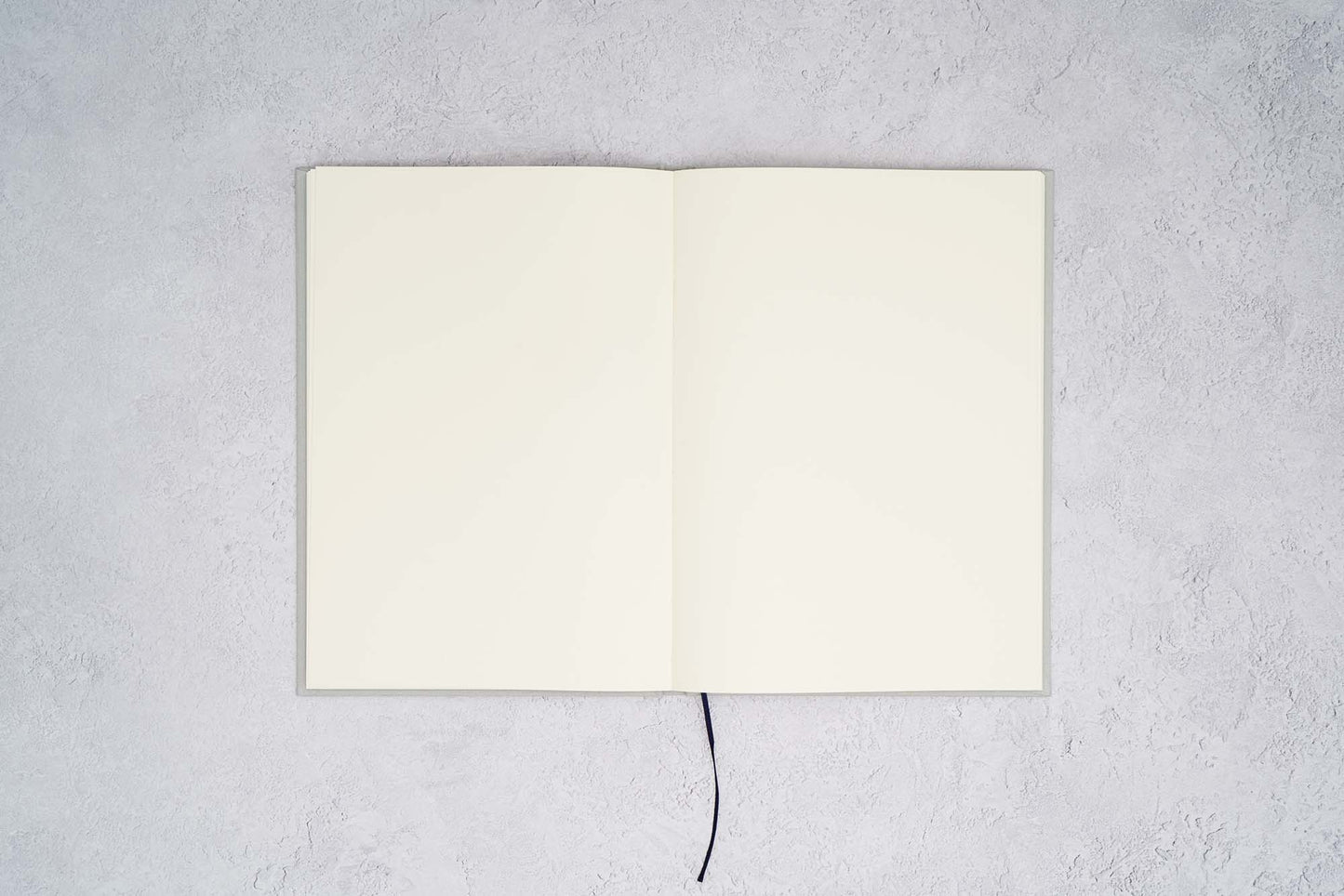 The Paper Mind Passepied Cream Hardcover Journal. Fountain pen friendly Journal. Light Gray Japanese Linen Cover. Notebook open with blank pages on gray concrete background.